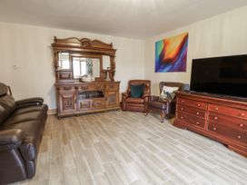 A living room with a sofa, armchair, cabinets, and television at Ty-Gan Dderwen in Llangennech