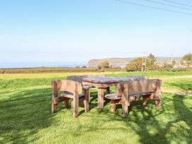 A table and benches on grass with a view of the ocean at Ty Felin Newport