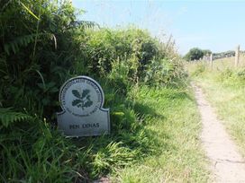 A sign indicating Pen Dinas along a pathway with grass at Dinas Island Cottage Dinas Cross