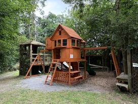 A playhouse with swings and a slide in an outdoor play area at Aeron in Newcastle Emlyn