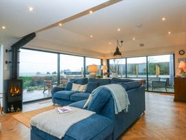 A living room with a wood stove and large windows at Bryn Mor Cottage in Mynytho near Llanbedrog