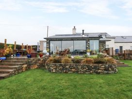 A garden with a stone wall and glass conservatory at Bryn Mor Cottage in Mynytho near Llanbedrog