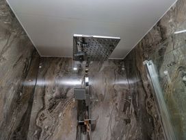 A shower with a rain shower head and marble walls at Little Hut in Grange-Over-Sands