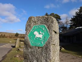 A sign for Dartmoor National Park near stone and trees at Swallows Nest in Widecombe-in-the-Moor near Postbridge