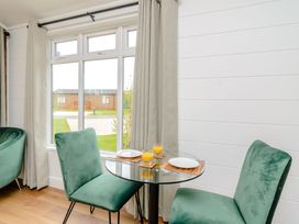 A dining room with a glass table and green chairs at The Castor in Kings Cliffe