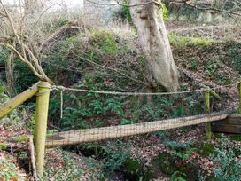 A suspension bridge over a creek surrounded by trees and ferns at Ty Uchaf in Colwyn Bay