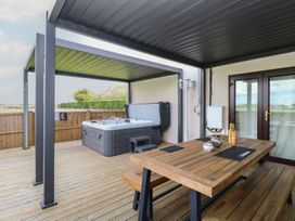 An outdoor seating area with a hot tub and wooden table at Aloe Lodge in Banham