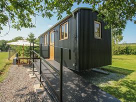 A shepherd's hut with steps and a table under an umbrella at Dave’s Place Broadstone near Munslow