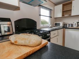 A kitchen with a gas stove and a loaf of bread on a cutting board at Swanage Coastal Park Caravan in Swanage