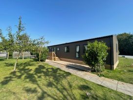 A mobile home with a deck and trees at Acacia Waterside Spa Carlton Miniott near Thirsk
