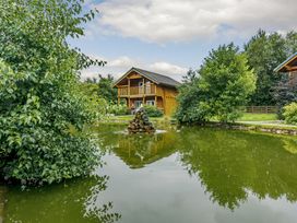 A house near a pond and trees at Birch Waterside Spa (Pet) Carlton Miniott near Thirsk