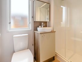 A bathroom with a toilet, sink, mirror, and shower at Cedar Spa (Pet) near Carlton Miniott