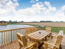 A deck with a wooden table and chairs overlooking water and field at Spindle Spa Carlton Miniott near Thirsk
