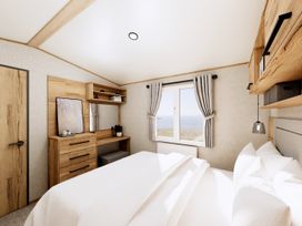 A bedroom with a bed, dresser, and window at Oak Waterside Spa (Pet) Carlton Miniott near Thirsk