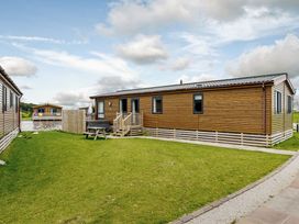 An outdoor view of a log cabin with a deck at Larch Waterside Spa Carlton Miniott near Thirsk