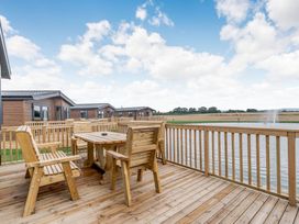 An outdoor area with wooden furniture and a view of a pond at Beech Waterside Spa (Pet) Carlton Miniott near Thirsk