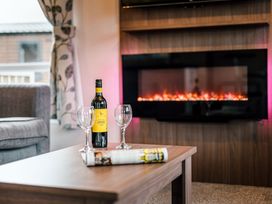 A living room with a sofa, table, wine bottle and glasses at Larch Waterside Spa (Pet) Carlton Miniott near Thirsk