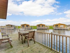 A wooden deck with a table and chairs overlooking water at Larch Waterside Spa (Pet) Carlton Miniott near Thirsk