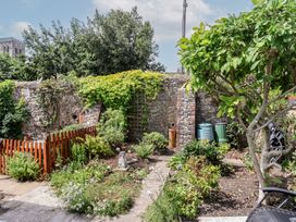 A garden with plants, a wall, and several water butts at Garden Studio at Stanley House Charmouth