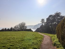 A path through grass with trees and ocean cliffs in the background at Fluta Seaton