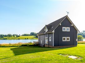 A house near a lake with grass and trees at Lochside Premier Spa in Dundee