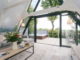 A living room with a sofa and coffee table leading to a deck with a jacuzzi at Glass Lodge in Praze-An-Beeble