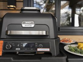 A woodfire grill with food items on a platter in an outdoor cooking area at Lowarth Lodge Spa Pet, Praze-An-Beeble