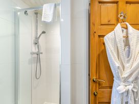 A bathroom with a shower and a robe hanging on the door at Caldew Cottage Spa in Penrith
