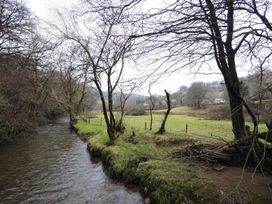 A view of a river bordered by trees and a grassy field at Nethercote Byre Minehead