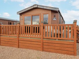 A wooden cabin with a deck and railing at Lakeside Lodge in Stonham Aspal