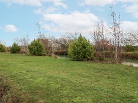 A grassy area near water with shrubs and trees at Lakeside Lodge in Stonham Aspal