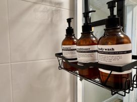A bathroom with shampoo, conditioner, and body wash on a shelf at Cotswolds Farmhouse Cottage
