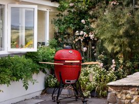 A grill on a patio with plants and a window at Whalesborough Farmhouse Spa Marhamchurch
