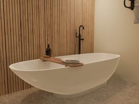 A bathroom with a bathtub and wooden accents at Kew Villa (Pet) Marhamchurch