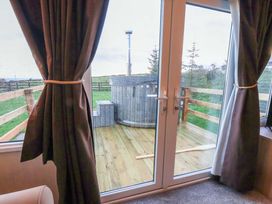 A view through glass doors with curtains towards a hot tub and decking at Swift Cabin in Scarborough