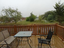 A deck with a table and chairs overlooking grass and trees at Fern Lodge in Stowmarket
