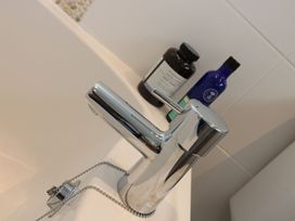 A faucet and bottles on the edge of a bathtub at Driftwood Cottage in Helston