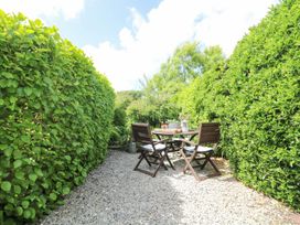 A garden with a table and chairs surrounded by hedges at Driftwood Cottage in Helston