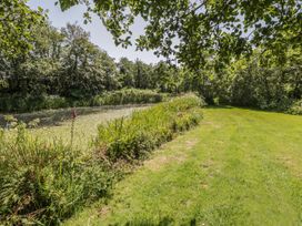 A grassy area beside a pond surrounded by trees at Falconers Cottage