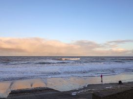 A beach scene with waves and a person walking with a dog at Paws By The Sea Norwich