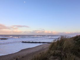 A beach with waves and grass near the shore at Paws By The Sea in Norwich