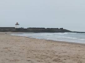 A beach with a lighthouse and ocean waves at The Retreat Cabin in Llanelli