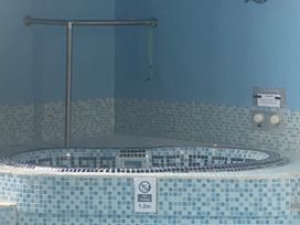 A bathtub with mosaic tiles and a handrail at Honeypot Cottage Whitchurch Canonicorum