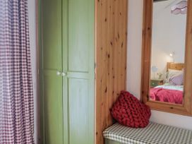 A bedroom with a wardrobe, mirror, and bench at Honeypot Cottage Whitchurch Canonicorum