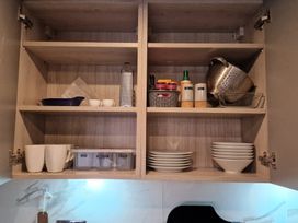 A kitchen cabinet with cups, plates, and storage containers at Birdsong lodge near Hawthorn Farm near Sutton-On-Sea