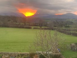 A sunset over mountains and a field with trees at Bluebell Shepherd’s Hut in Llanfairpwllgwyngyll