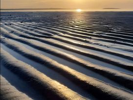 A sandy beach with water and sunset at Sea view cottage in Penmaenmawr
