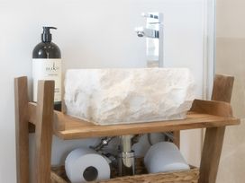 A stone basin on a wooden shelf with a faucet at Honey Bee Cottage in Welshpool
