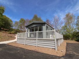 A log cabin with decking and railings surrounded by trees at No.6 - The Pines in Delamere