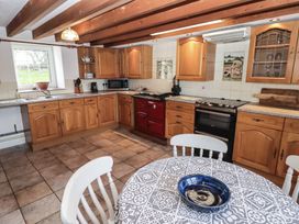 A kitchen with wooden cabinets and a round dining table at Rhosgranog Cottage in Llandeloy near Solva